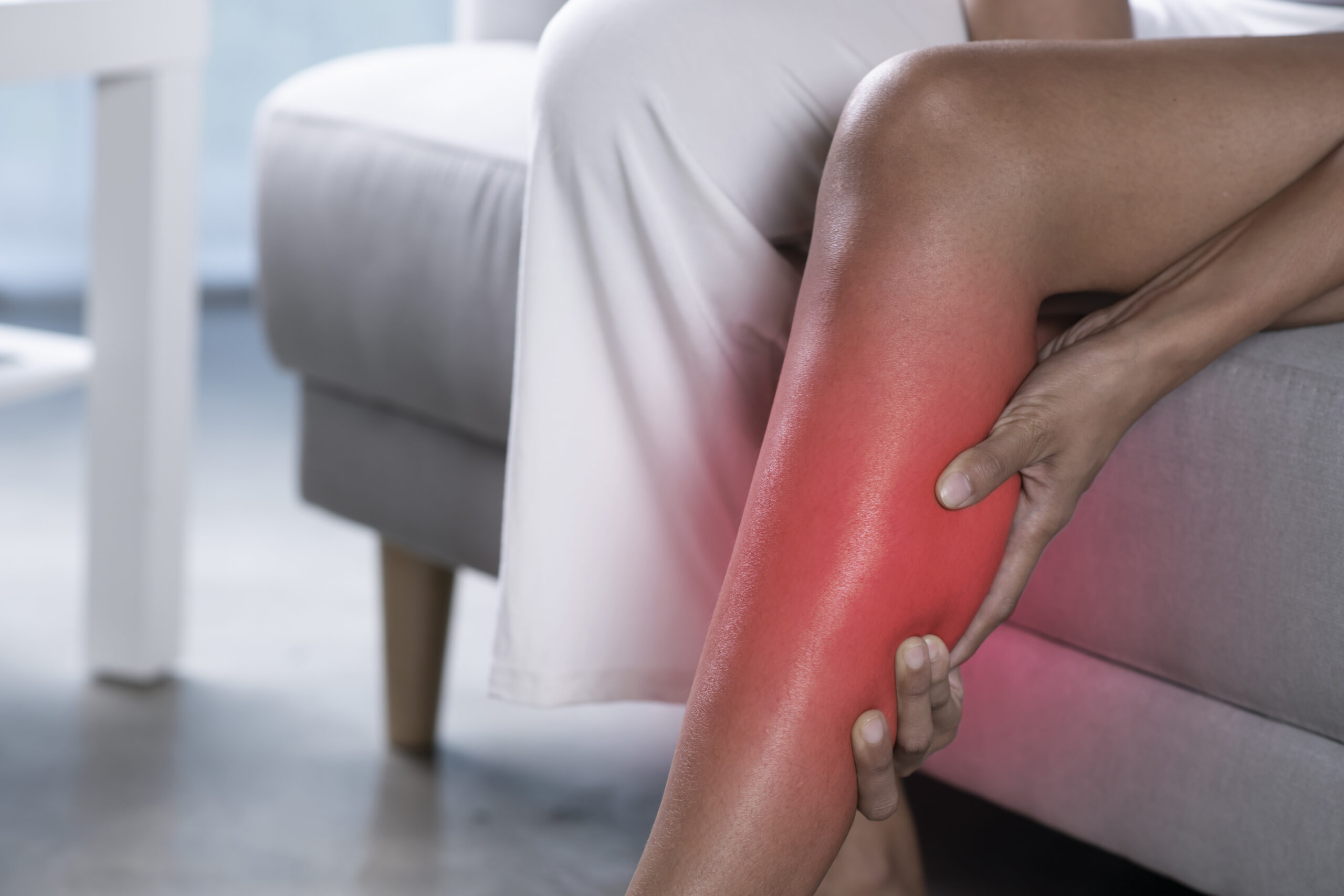 Asian woman holding the calf with pain. Close-up image of female suffering from pain in leg at home. Health care concept.